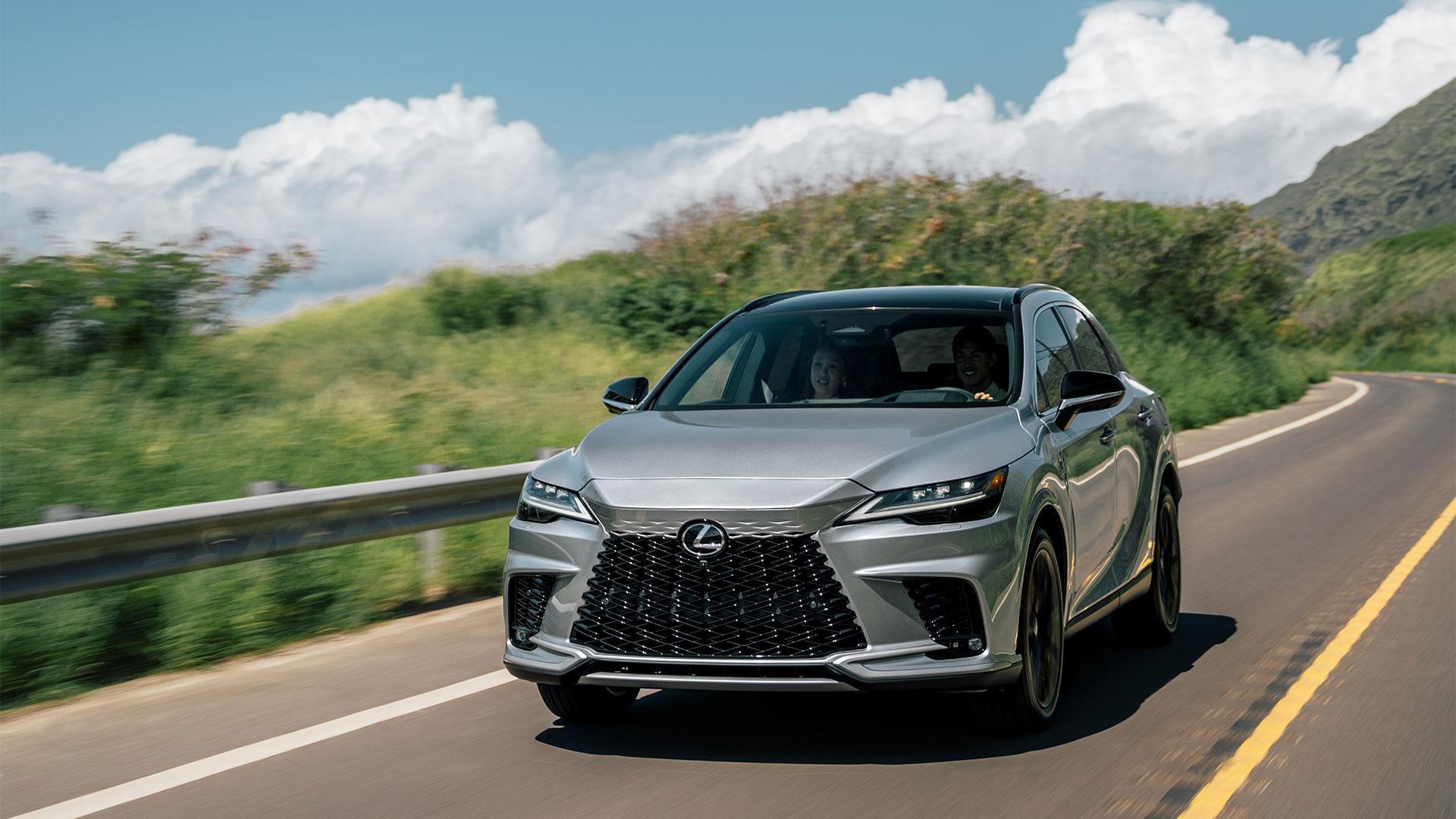 2025 Lexus RX 350 Hybrid Iridium driving through grassy hills and mountains on a clear sunny day.