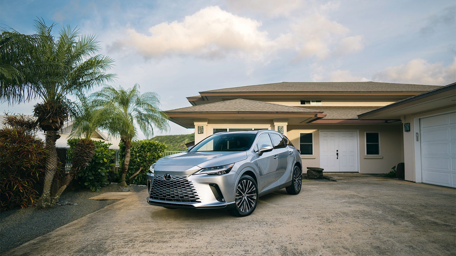 2025 Lexus RX Hybrid 350 Iridium parked in driveway of home next to palm trees and hedges.